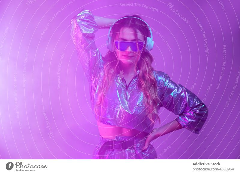 Futuristic female in stylish outfit standing in studio with neon illumination woman illuminate listen appearance style futuristic headphones 80s personality