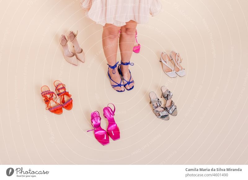 Stylish girl standing in pink pleated dress surrounded by a variety of shoes. She is dressed in a pink pleated skirt, on her feet blue shoes. Shoes assortment