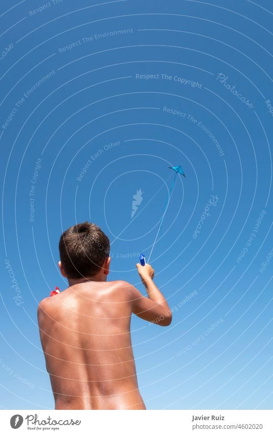 boy on his back playing with a stunt kite seen from below with the kite high up in the blue sky on a summer day, copy space acrobatic child flying