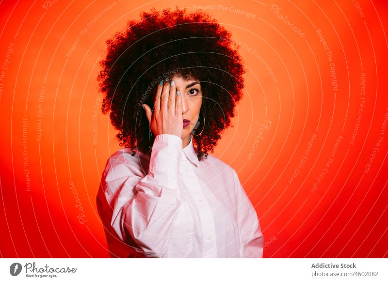Confident ethnic lady covering eye with hand in red studio woman cover eye self assured trendy serious confident half of face portrait model individuality