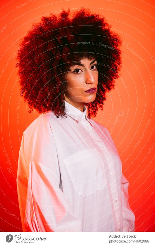 Serious Hispanic lady standing in studio with neon red lights woman serious model portrait appearance style confident self assured gorgeous emotionless fashion