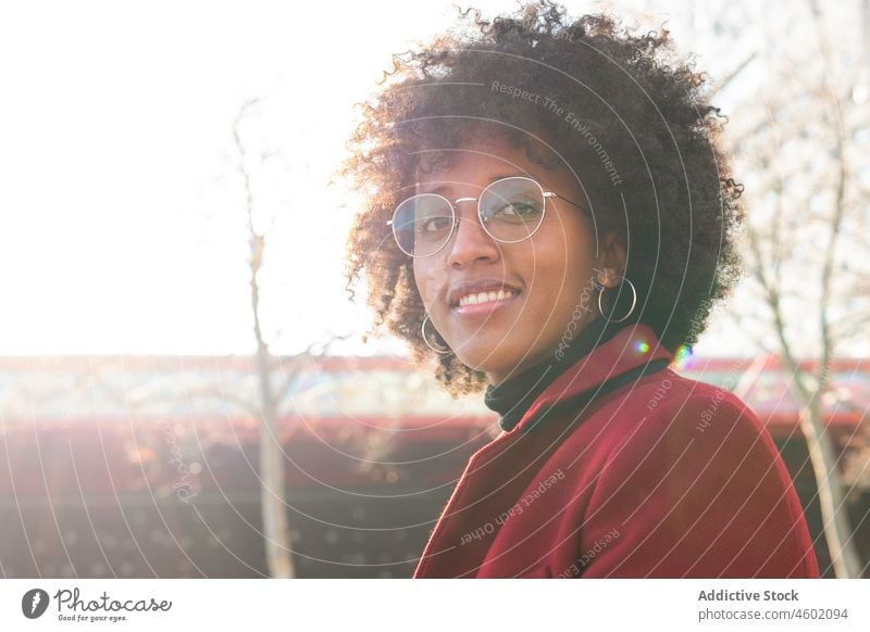 Smiling African American woman in crimson coat and eyeglasses afro hairstyle positive curly hair casual portrait cheerful sunlight smile happy charming optimist