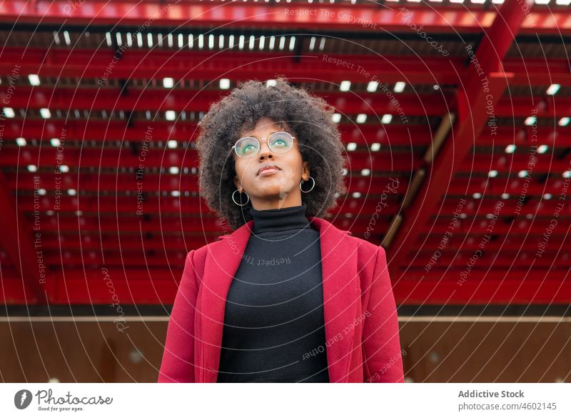 African American woman in crimson coat and eyeglasses afro hairstyle positive curly hair casual portrait charming optimist human face carefree eyewear trendy