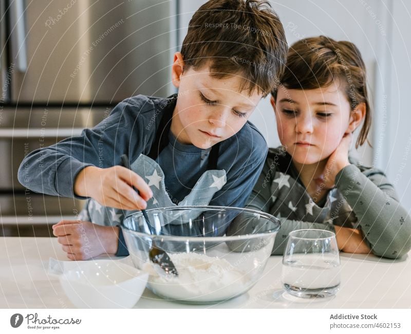 Cheerful siblings mixing dough together in kitchen cook boy girl culinary flour love children kitchenware brother sister homemade stir bowl pastry apron happy