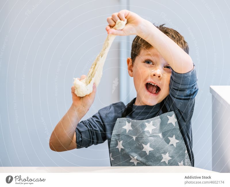Cheerful boy with dough in kitchen cook kid flour knead pastry having fun helper tear apron process bake food domestic child kitchenware culinary product messy