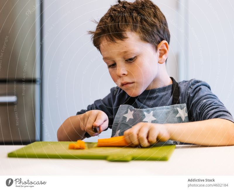 Focused boy cutting carrot in kitchen cook kid culinary child at home food helper slice prepare kitchenware process chop vitamin fresh ingredient knife yellow
