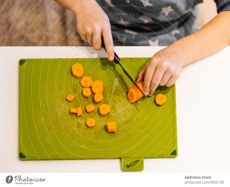Anonymous boy cutting carrot in kitchen cook kid culinary child at home food helper slice prepare kitchenware process chop vitamin fresh ingredient knife yellow