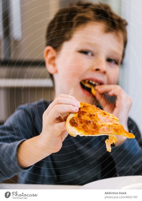 Cheerful boy eating pizza in kitchen kid child kitchenware domestic at home food meal piece hungry cuisine pleasure enjoy pastry yummy fast food homemade lunch