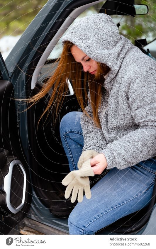Woman sitting on driver seat and putting on gloves car woman winter auto put on warm clothes hood road trip parked stuck casual window open door outfit weather