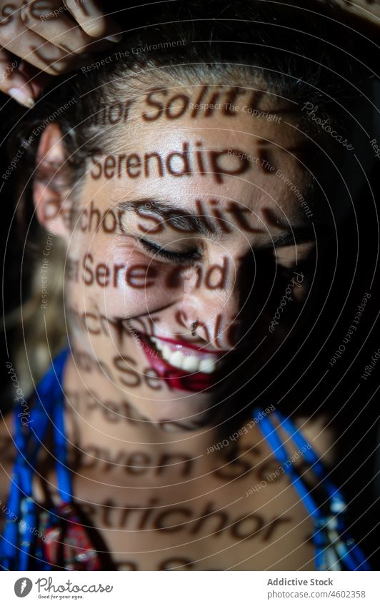 Cheerful woman with inscriptions on face projector portrait solitude serendipity illuminate concept cover face word female text toothy smile effect young