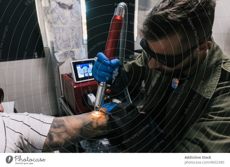 Master making laser tattoo on hand of man men salon make master client professional work machine male concentrate ink focus pain art procedure tool create job