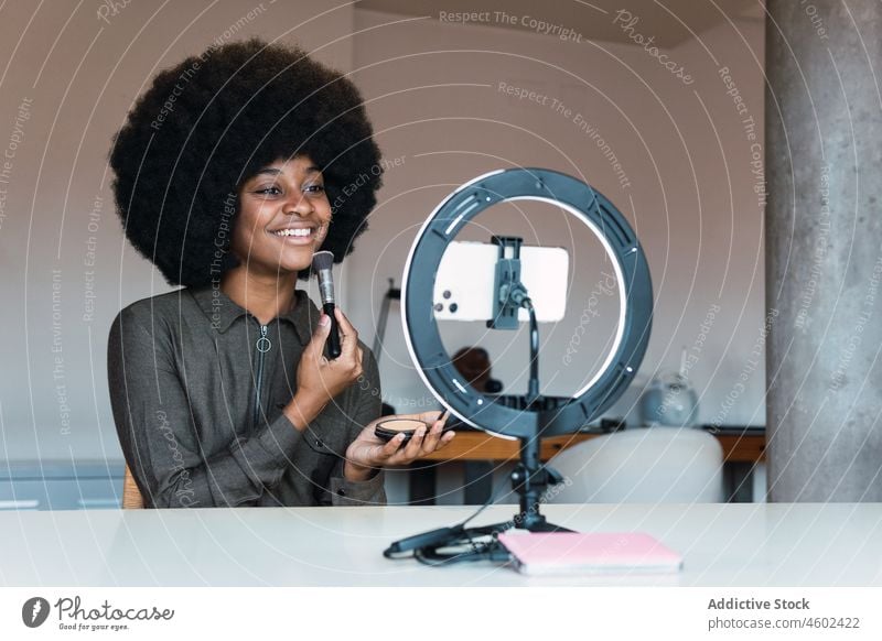 Black woman recording beauty video makeup tutorial cosmetic vlog smartphone ring lamp powder blog social media online afro leisure hairstyle feminine blogger