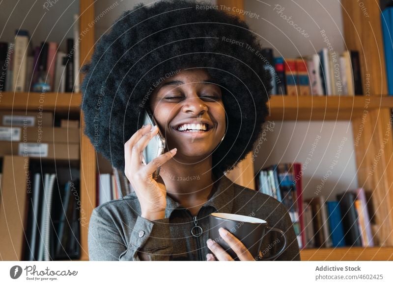 Cheerful black woman with coffee talking on smartphone phone call conversation discuss hot drink beverage afro smile chat leisure hairstyle feminine appearance