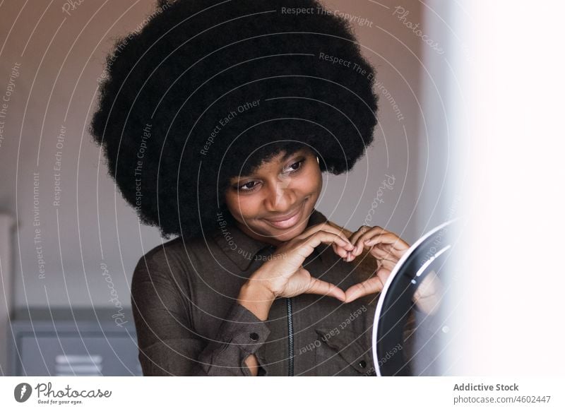 Smiling black woman showing heart gesture through ring lamp blogger love vlogger leisure smile afro hairstyle feminine appearance happy charming brunette