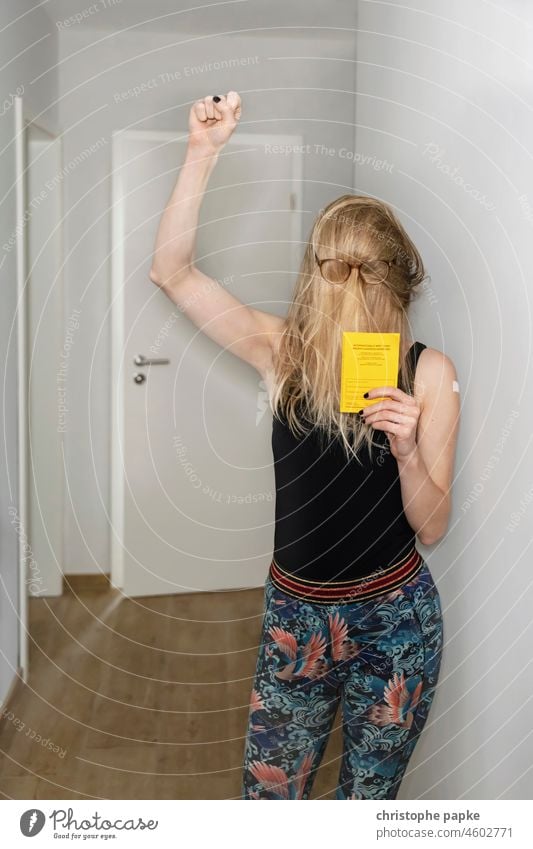 Woman with glasses over hair holds vaccination card in her hand and enjoys it Blonde Immunization corona Protection foolish Joy COVID pandemic Corona virus