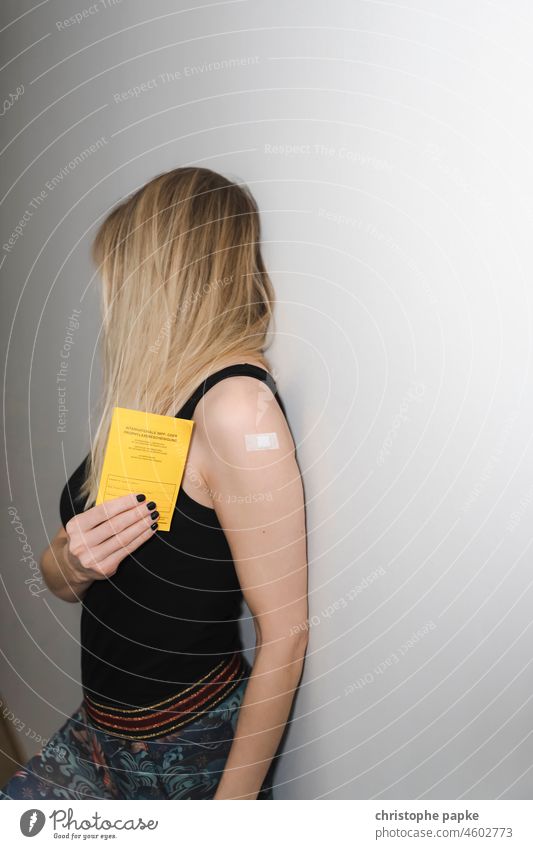 Woman with patch on upper arm holds vaccination card in hand Blonde Immunization corona Protection foolish Joy COVID pandemic Corona virus Healthy Virus