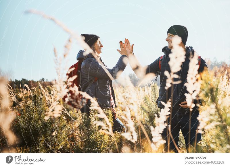 Friends enjoying trip in nature, giving high five while vacation day. Hikers with backpacks on way to mountains. Walking through tall grass along path in meadow on sunny day