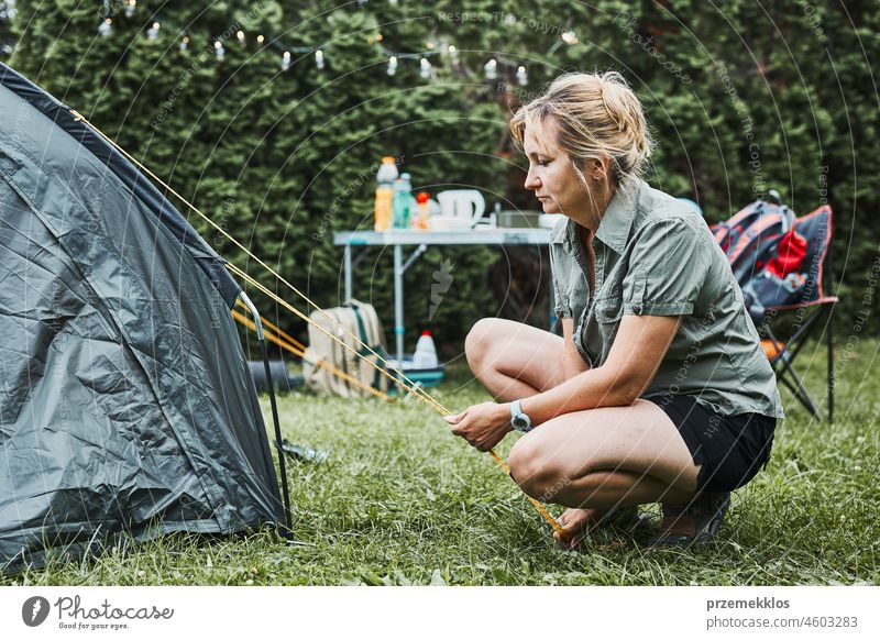 Woman putting up a tent at camping during summer vacation. Female preparing campsite to rest and relax trip adventure traveling active recreation equipment