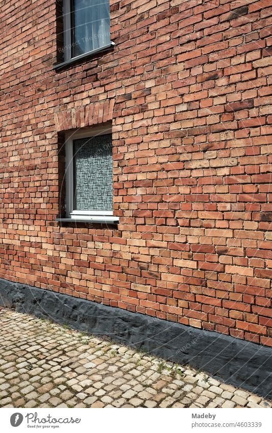 Window with fluted glass and curtain in an old red-brown clinker facade of a farmhouse with grey cobblestones in summer sunshine in Alverdissen near Barntrup in Ostwestfalen-Lippe, Germany