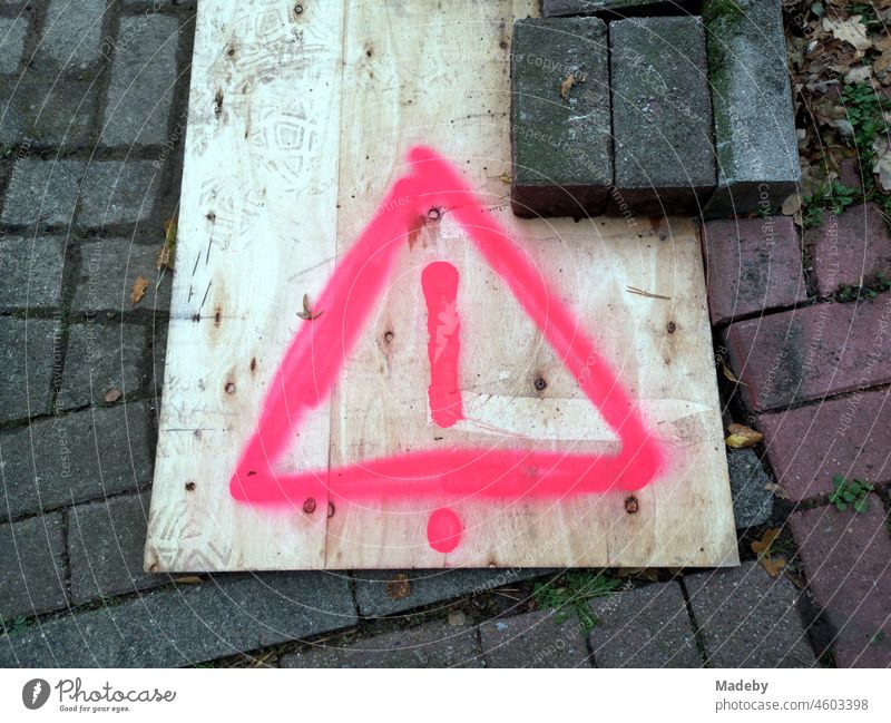 Wooden plate in beige with painted warning sign in pink above a building pit on the pavement in Steinhude at the Steinhuder Meer near Wunstorf in the district of Hannover