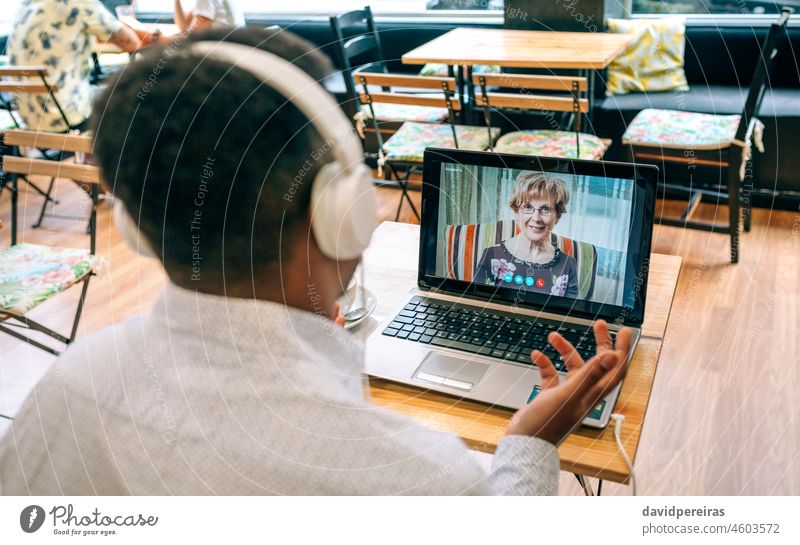 Man talking on video call with his mother from a cafeteria unrecognizable man laptop internet headphones screen person videoconference male table family sitting