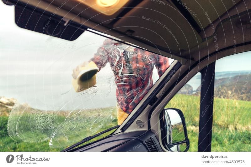 Man cleaning camper van windshield outdoor unrecognizable man soaping glass sponge view from inside through the glass outdoors careful owner perfectionist rub