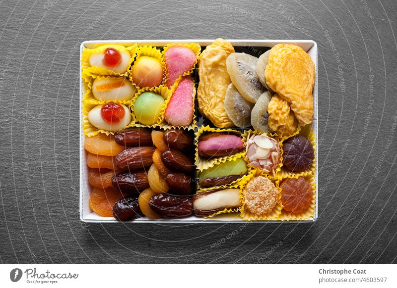 Slate tray with on it's middle, a white metal dish with candies and dried fruits. Studio Shot White Color full frame food photography Candy apricot kiwi mango