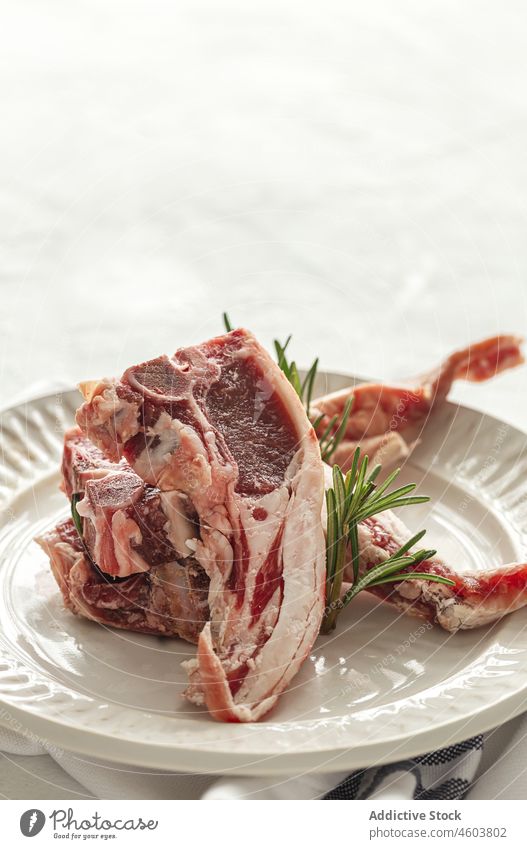 Raw lamb chops on plate raw meat serve rosemary uncooked food herb culinary table fresh delicious tasty ceramic kitchen cuisine ingredient light palatable