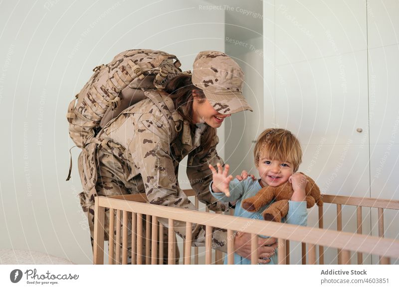 Caring military woman holding son mother smile soldier crib bedroom army duty patriot boy child cute love delight together childcare childhood home uniform