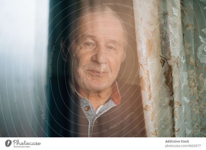 Calm pensive elderly man behind window senior age room portrait pensioner grandparent solitude alone home curtain light calm aged mature at home gray hair