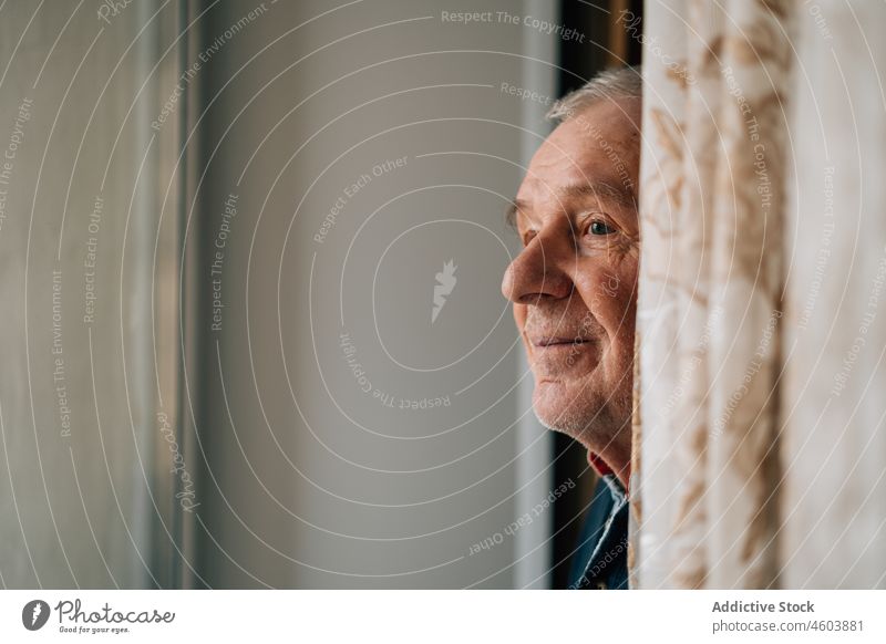 Elderly man standing near window elderly senior age room portrait pensioner grandparent solitude alone home curtain light calm aged mature at home gray hair