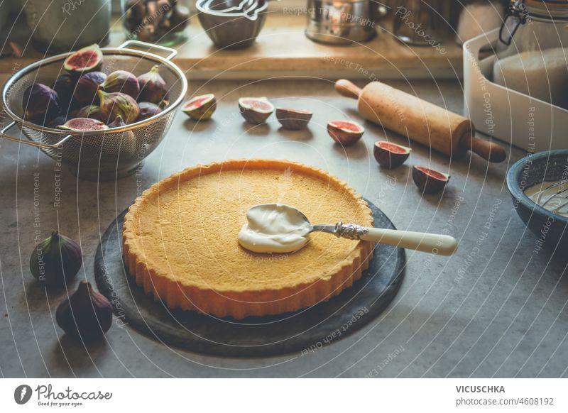 Sweet tart crust with spoon, cream and figs on kitchen table with baking tools at window sweet bake bakery cake cuisine dough filling food fruit home homemade