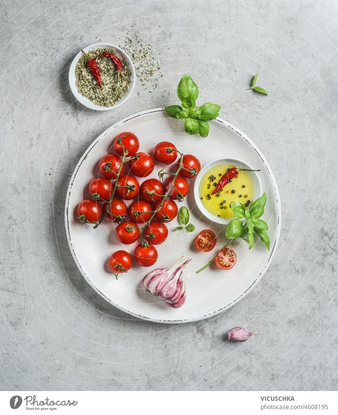 Fresh tasty ingredients: tomatoes, bowl with olive oil,herbs,garlic and green salt with chili pepper on white plate. Top view fresh top view appetizer