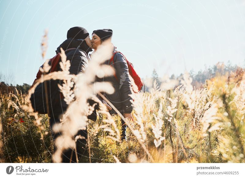 Couple sharing a passionate kiss while vacation trip. Hikers with backpacks standing on trail. People walking through tall grass along path in meadow on sunny day