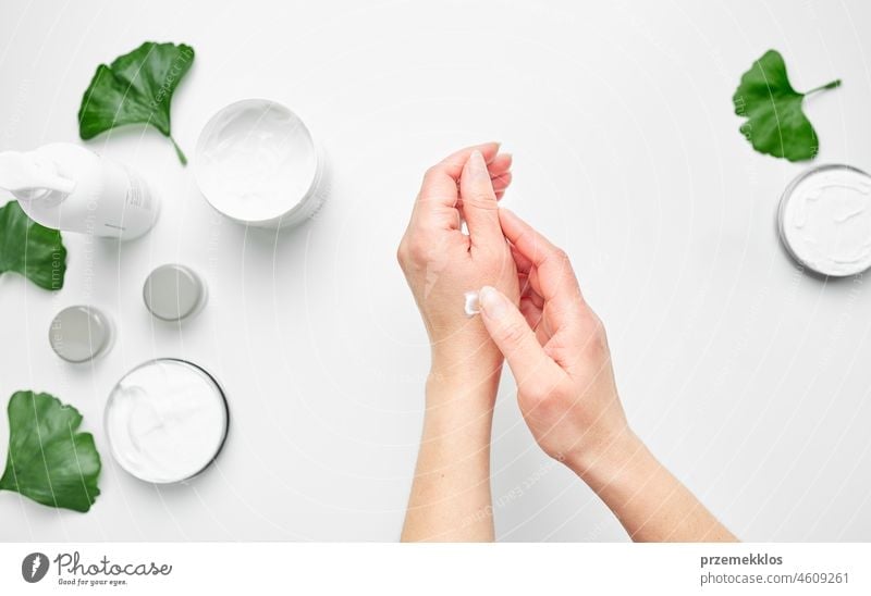 Woman applying  cosmetic moisturizing hand cream. Cosmetic products, green leaves on white table. Spa, manicure, skin care concept nail woman beauty moisturizer