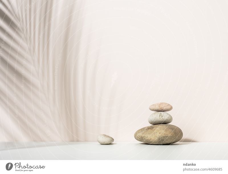 stack of round stones and and the shadow of a palm leaf on a beige background. Scene for demonstration of cosmetic products, advertising backdrop beauty blank