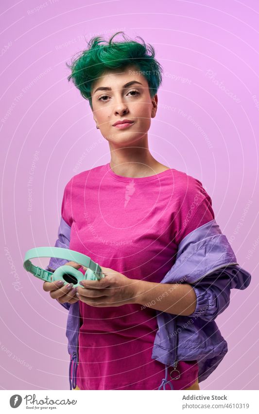 Charismatic woman with headphones in retro outfit meloman style millennial 80s fashion design music song listen audio studio green hair female model short hair