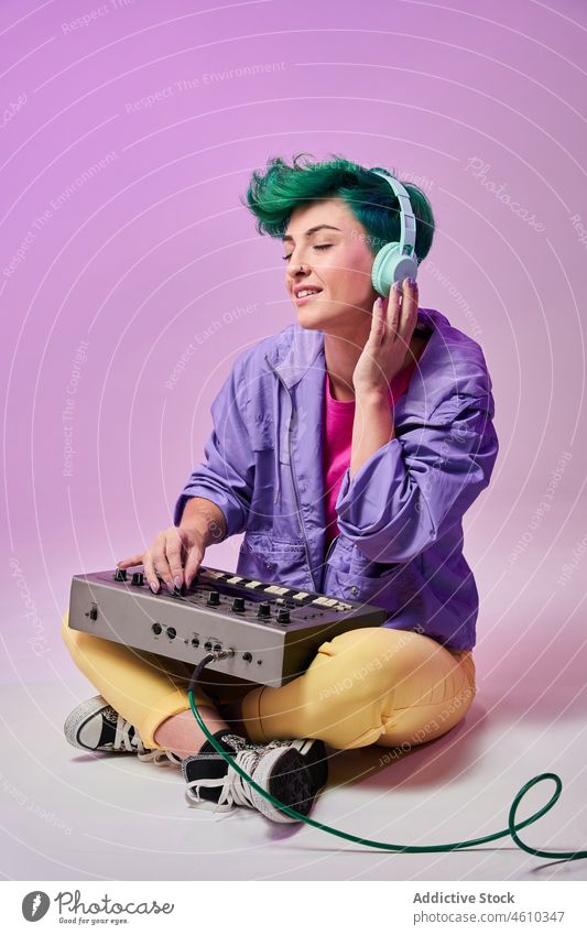 Content millennial woman in headphones playing on keyboard controller compose 80s music musician style fashion design retro song audio studio green hair female