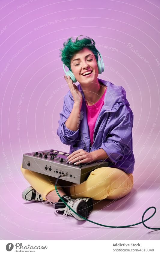 Positive millennial woman in headphones playing on keyboard controller compose 80s music musician style fashion design retro song audio studio green hair female