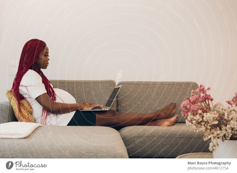 Black pregnant woman relaxing on sofa at home with his laptop abdomen adult anticipation baby belly birth business care chinese computer couch expecting family