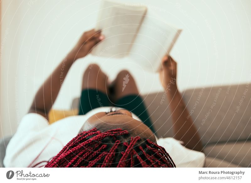 Black woman laying on the sofa reading a book with his feets on the wall adult african attractive background beautiful beauty black woman cheerful comfort
