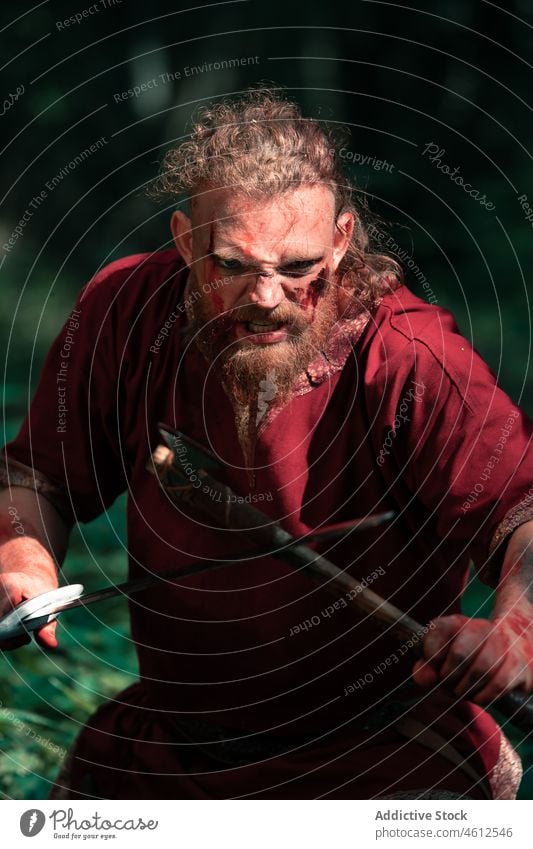 Aggressive viking with axe and sword fighting in forest man angry shield scream aggressive attack reenactment battle male violent scandinavian warrior