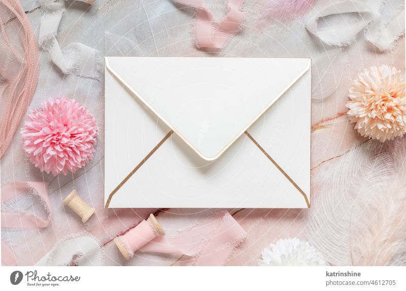 White envelope between pastel flowers, silk ribbons and feathers on marble WEDDING mockup Flowers pink top view girlish White paper valentine spring mothers day