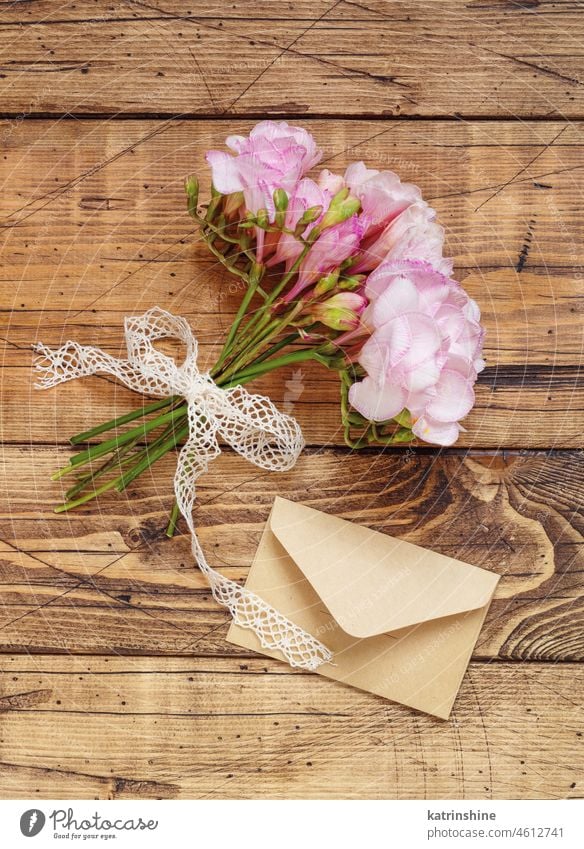 Bouquet of beautiful freesia flowers with ribbon and envelope  top view. Mockup on wooden table bouquet holiday mockup pink birthday celebration flat lay