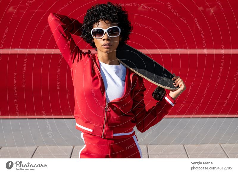 African American woman with short hair, sunglasses and red sportswear with her skateboard African-American youthful Young woman more adult mature woman