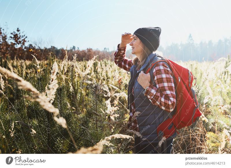 Young woman enjoying the view of mountains. Woman standing on trail and looking at view. Woman with backpack hiking through tall grass along path in mountains