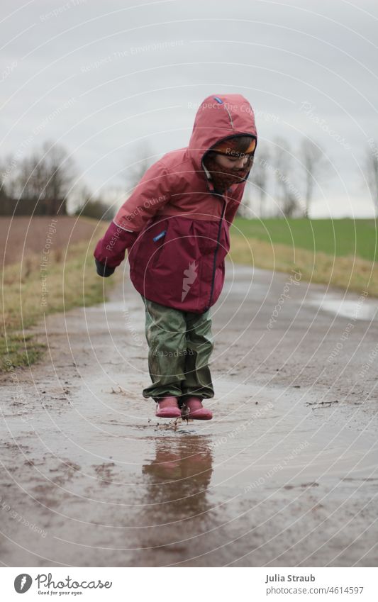 Girl in rubber boots floats over giant puddle Puddle Rainy weather rainwear slush pants Autumn Winter being out play outdoors Childhood memory Infancy