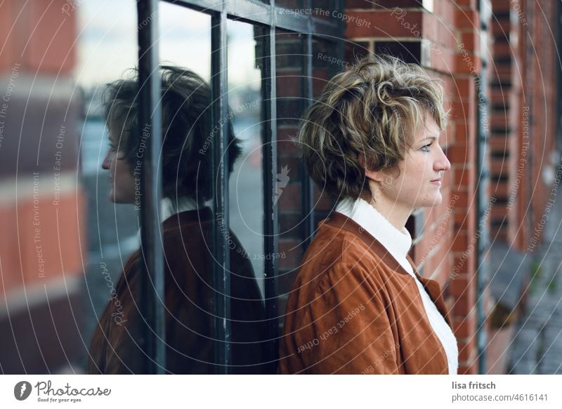 WAITING - LONGING - MIRROR IMAGE Woman Blonde Short-haired Curl Adults Colour photo Exterior shot Day Mirror image Longing Window Brick facade Brick wall