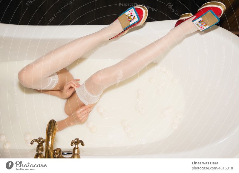 A milk bath for this gorgeous fashion model. Her legs are long and pretty. She’s wearing red shoes with some gold and playing cards. A milk bath is a place for such a beautiful creature to be.