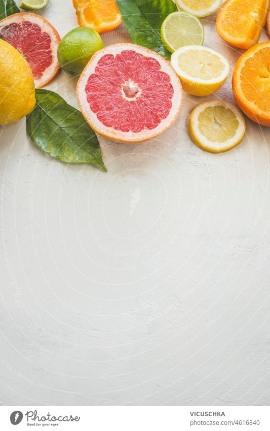 Citrus fruits halves background on white table: grapefruit, orange, lime and lemon. Healthy vitamin c rich fruits with green leaves. Top view with copy space.